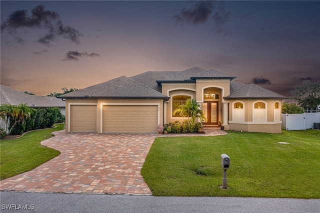 view of front of property featuring a garage, a lawn, fence, decorative driveway, and stucco siding