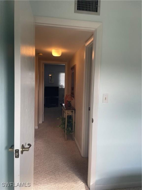 corridor with baseboards, visible vents, and light colored carpet