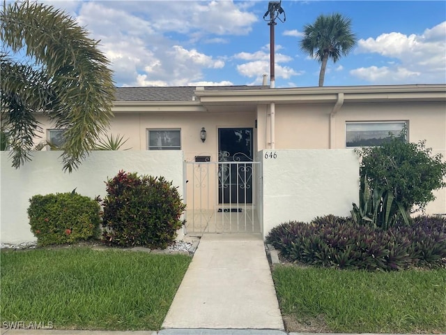 property entrance featuring a gate, fence, and stucco siding