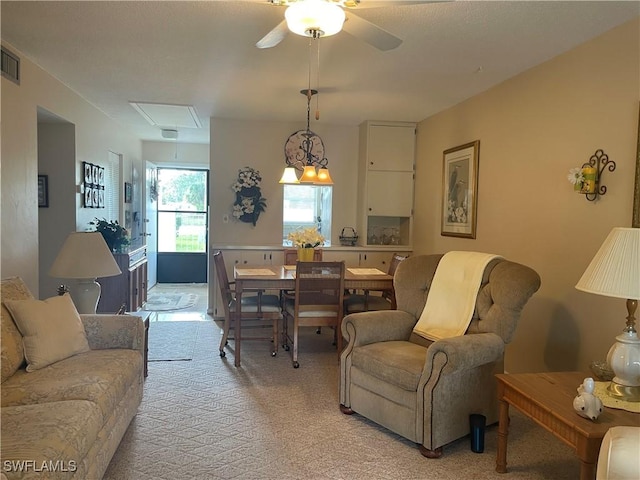 living room with light carpet, ceiling fan, visible vents, and attic access