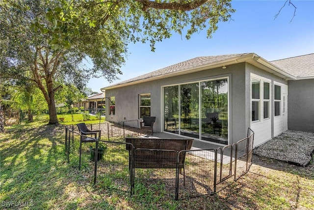 rear view of house with a lawn, fence, and stucco siding