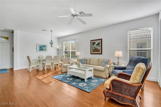 living area featuring baseboards, ceiling fan, visible vents, and wood finished floors