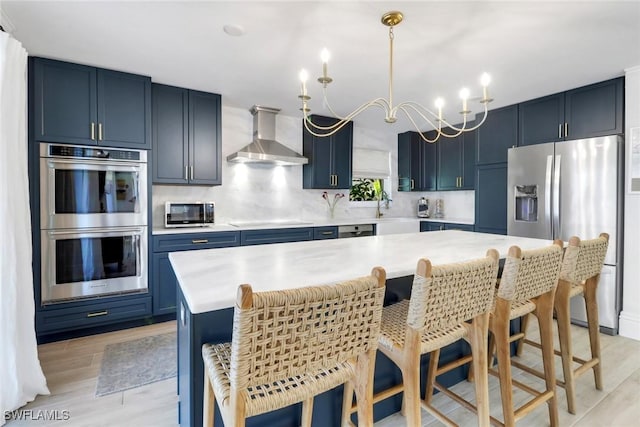 kitchen featuring appliances with stainless steel finishes, light countertops, blue cabinets, and wall chimney exhaust hood