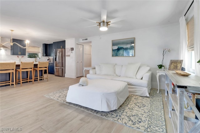 living area with light wood-style floors, visible vents, and ceiling fan with notable chandelier