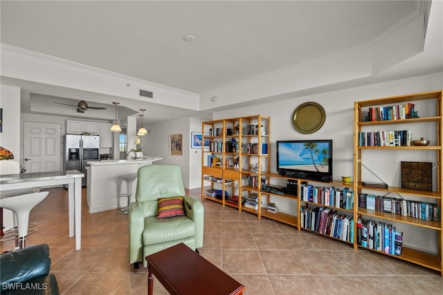 tiled living room with a tray ceiling, visible vents, and crown molding