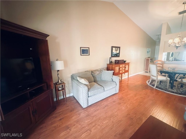 living area featuring a chandelier, high vaulted ceiling, light wood finished floors, and baseboards