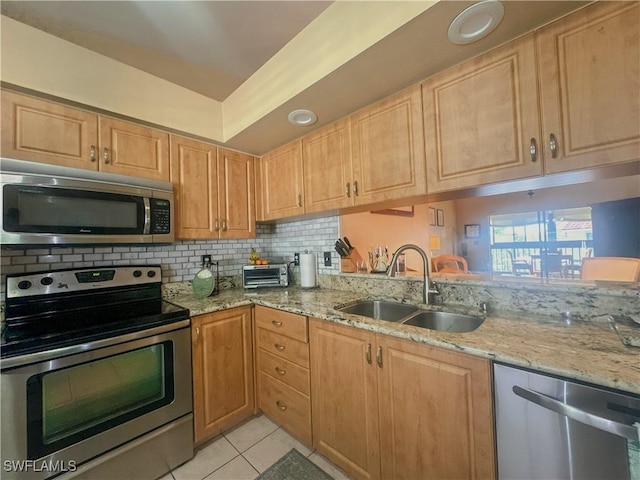 kitchen with light tile patterned floors, stainless steel appliances, a sink, decorative backsplash, and light stone countertops