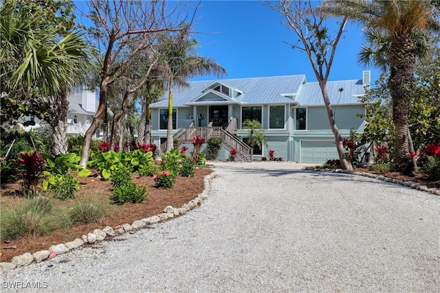 view of front of house featuring stairway, metal roof, gravel driveway, an attached garage, and a porch