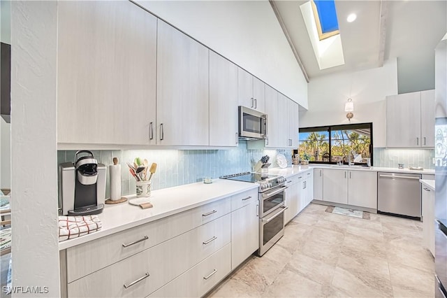 kitchen featuring a skylight, decorative backsplash, appliances with stainless steel finishes, light countertops, and a sink