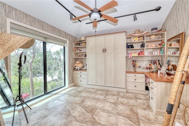 interior space featuring built in study area, ceiling fan, track lighting, and wallpapered walls