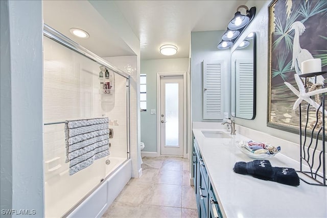 bathroom featuring double vanity, bath / shower combo with glass door, toilet, tile patterned floors, and a sink