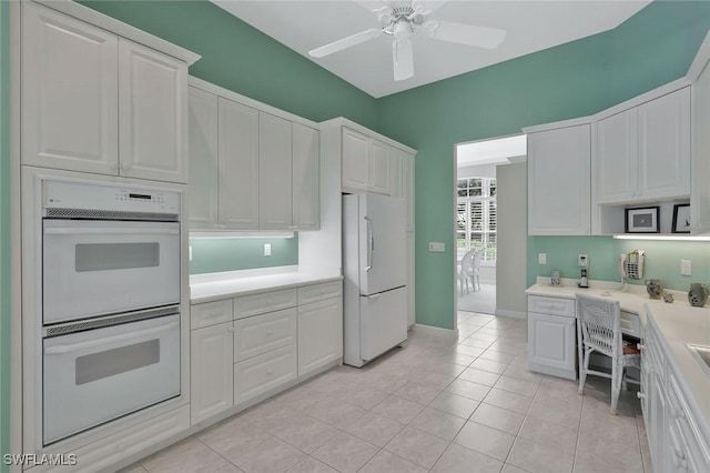 kitchen with white appliances, built in desk, light countertops, and white cabinetry