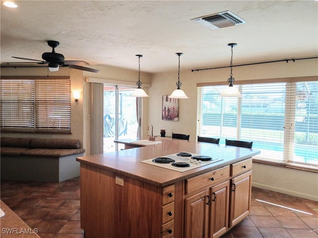 kitchen with pendant lighting, white electric stovetop, visible vents, a sink, and dark tile patterned flooring