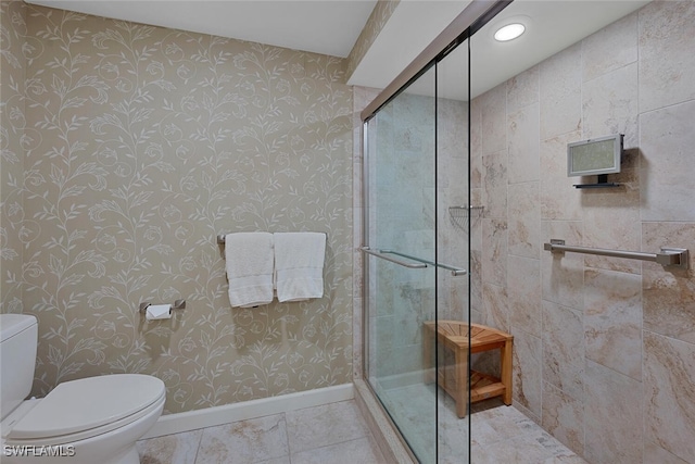 bathroom featuring toilet, tile patterned flooring, baseboards, and tiled shower