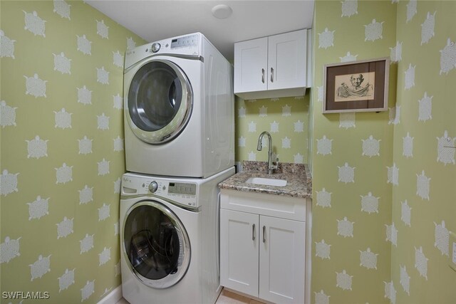 laundry room with stacked washer / dryer, cabinet space, a sink, and wallpapered walls