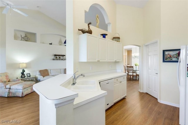 kitchen featuring arched walkways, white appliances, a sink, open floor plan, and light wood finished floors