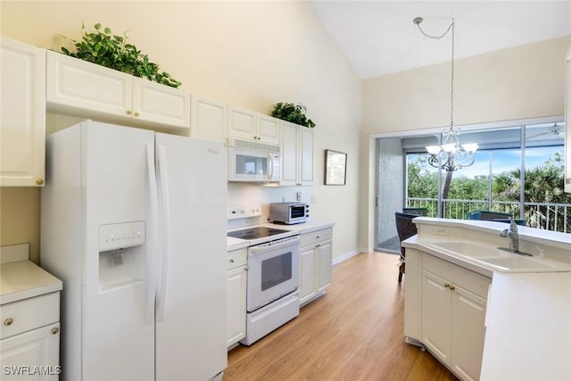 kitchen with white appliances, a sink, white cabinets, hanging light fixtures, and light wood finished floors