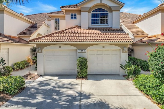 mediterranean / spanish-style house featuring driveway, an attached garage, a tiled roof, and stucco siding