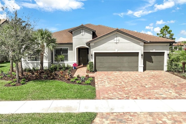 mediterranean / spanish-style house with a garage, a tiled roof, decorative driveway, stucco siding, and a front yard