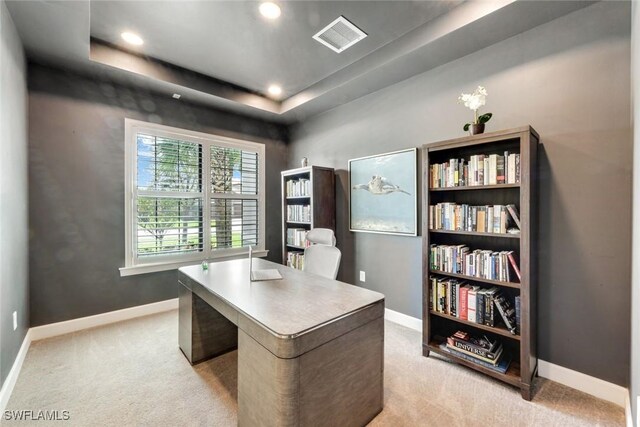 office area featuring baseboards, visible vents, a tray ceiling, and light colored carpet