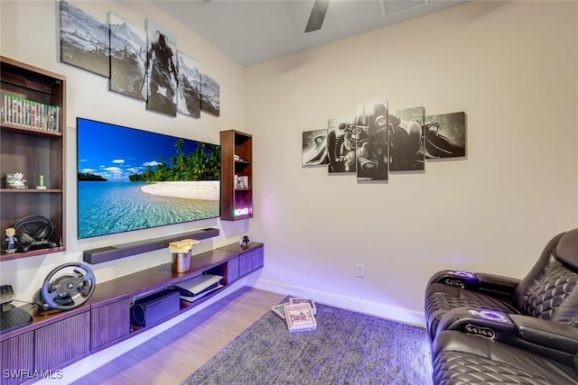 home theater room with a ceiling fan, baseboards, visible vents, and wood finished floors