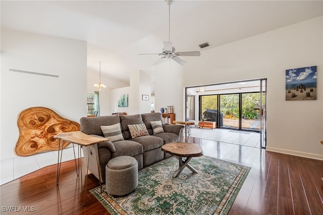 living area featuring baseboards, visible vents, hardwood / wood-style floors, high vaulted ceiling, and ceiling fan with notable chandelier