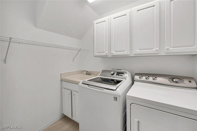 clothes washing area with light wood-style flooring, a sink, baseboards, cabinet space, and washer and clothes dryer