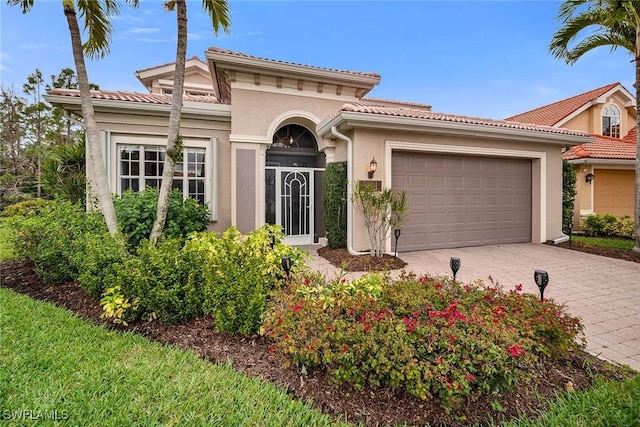 mediterranean / spanish house with a garage, a tiled roof, decorative driveway, and stucco siding