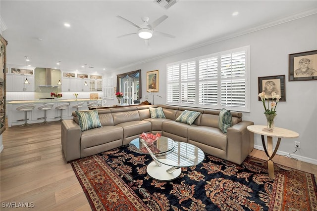 living room with light wood-style flooring, visible vents, ornamental molding, and ceiling fan