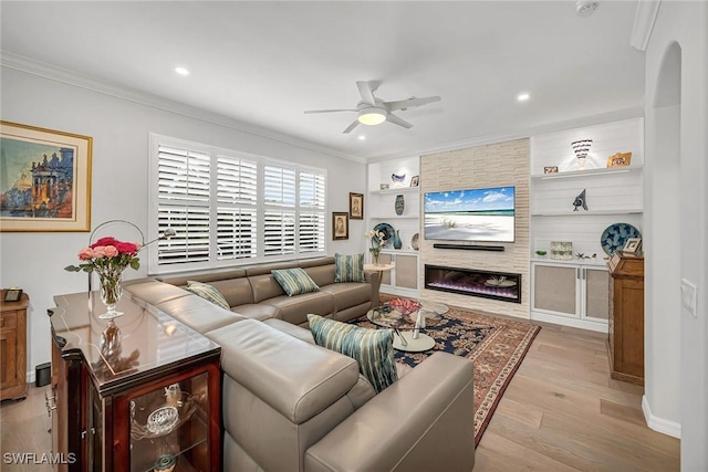 living room with ceiling fan, built in shelves, a fireplace, wood finished floors, and ornamental molding