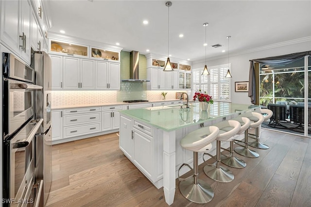 kitchen featuring gas stovetop, light wood-style floors, stainless steel double oven, ornamental molding, and wall chimney exhaust hood