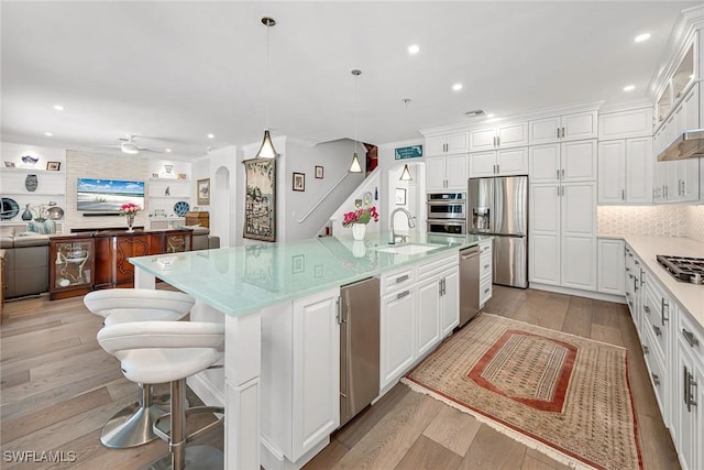 kitchen with arched walkways, stainless steel appliances, light wood-style flooring, and white cabinetry