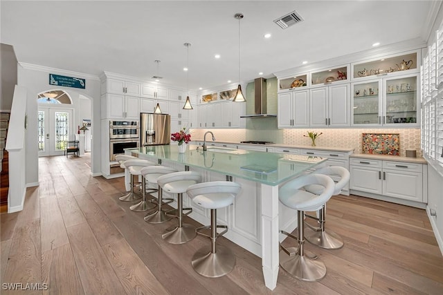 kitchen with french doors, visible vents, appliances with stainless steel finishes, a sink, and wall chimney range hood