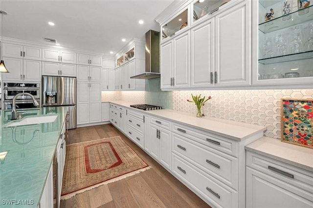 kitchen with white cabinets, wall chimney exhaust hood, stainless steel appliances, and wood finished floors