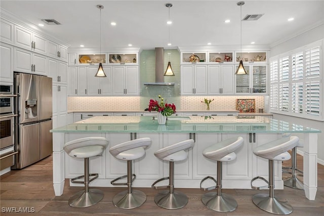 kitchen with appliances with stainless steel finishes, wall chimney range hood, white cabinetry, and tasteful backsplash