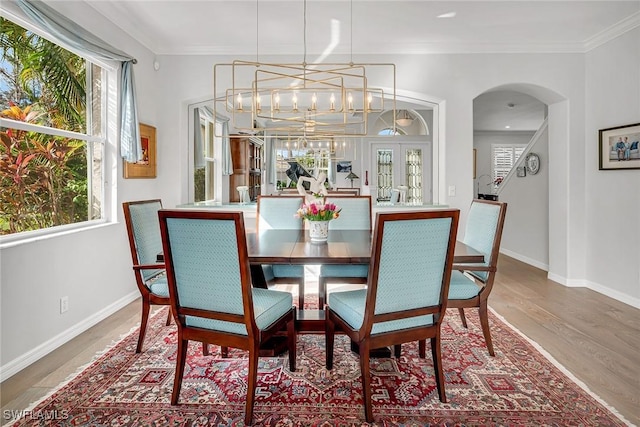 dining area featuring arched walkways, plenty of natural light, wood finished floors, and crown molding