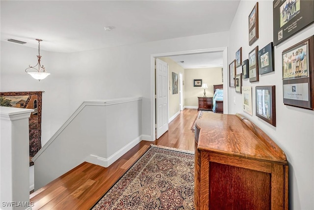 hallway featuring baseboards, visible vents, an upstairs landing, and wood finished floors