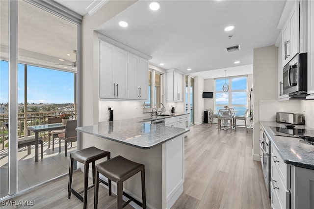 kitchen with visible vents, white cabinets, decorative backsplash, stainless steel microwave, and light wood-style floors