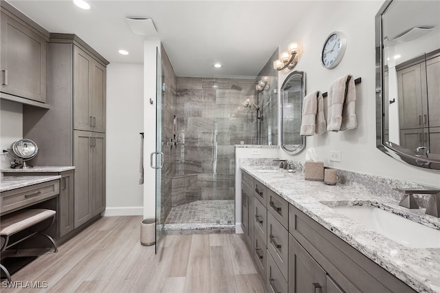 bathroom featuring double vanity, wood finished floors, a sink, and a shower stall