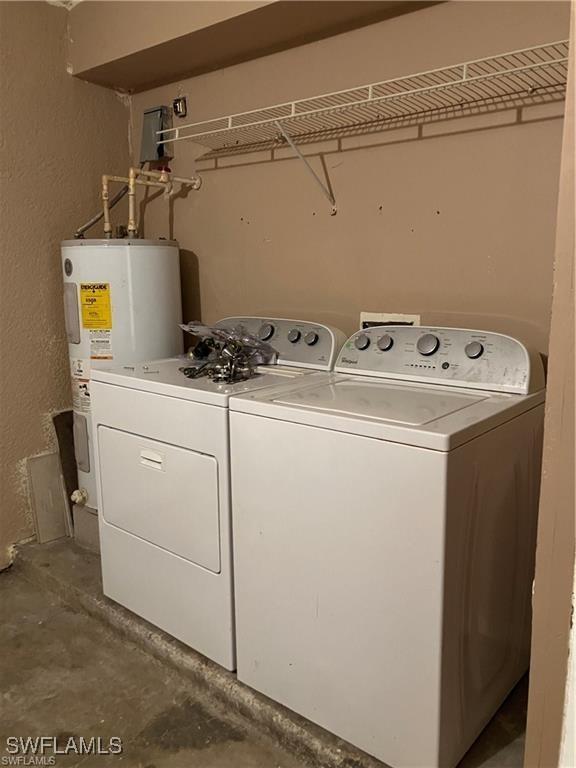 clothes washing area featuring water heater, a textured wall, washer and clothes dryer, and laundry area