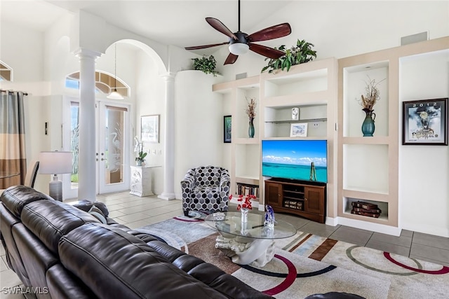 tiled living room featuring decorative columns, arched walkways, a ceiling fan, built in shelves, and high vaulted ceiling