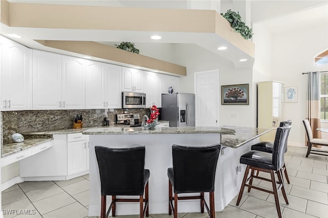 kitchen featuring light tile patterned floors, tasteful backsplash, a breakfast bar, stainless steel appliances, and white cabinetry