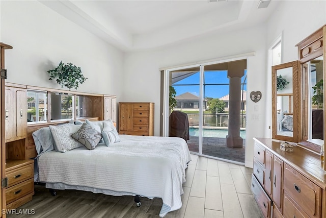 bedroom featuring light wood-style flooring, a raised ceiling, a towering ceiling, and access to exterior