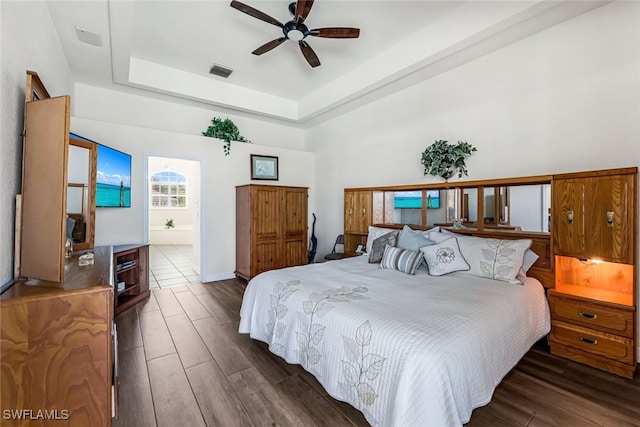 bedroom with ensuite bathroom, wood finished floors, visible vents, a ceiling fan, and a raised ceiling