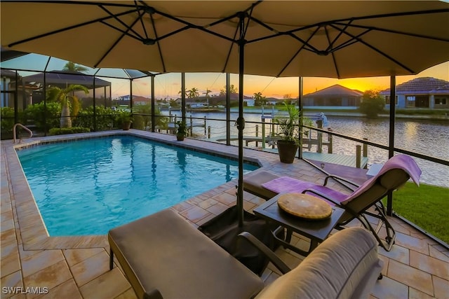 pool at dusk featuring a water view, glass enclosure, an outdoor pool, and a patio