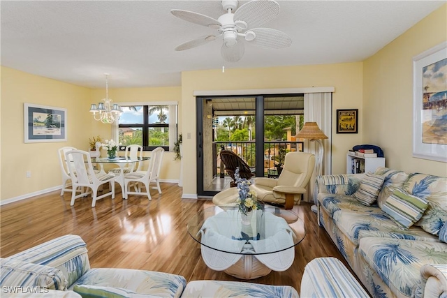 living area with baseboards, wood finished floors, and ceiling fan with notable chandelier