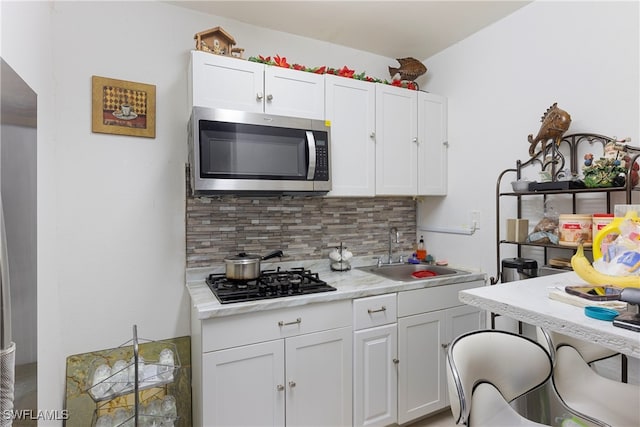 kitchen with tasteful backsplash, stainless steel microwave, white cabinetry, a sink, and black gas stovetop