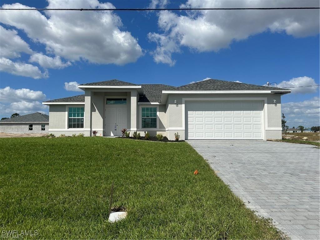 prairie-style home with an attached garage, a front lawn, decorative driveway, and stucco siding