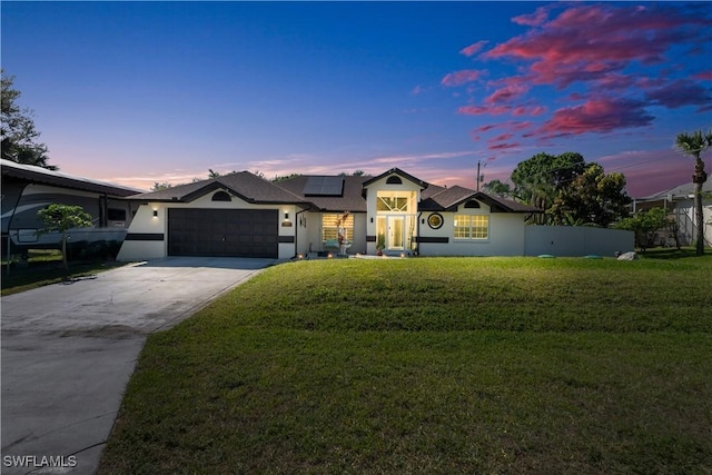 view of front of property with an attached garage, solar panels, fence, driveway, and a lawn