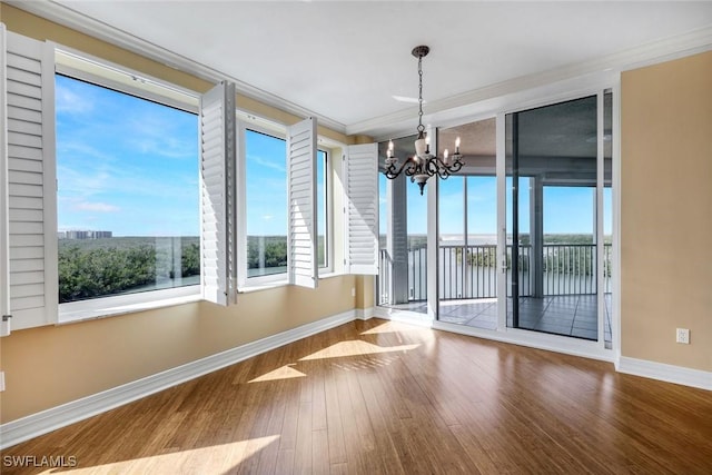 unfurnished dining area featuring ornamental molding, wood finished floors, baseboards, and a chandelier